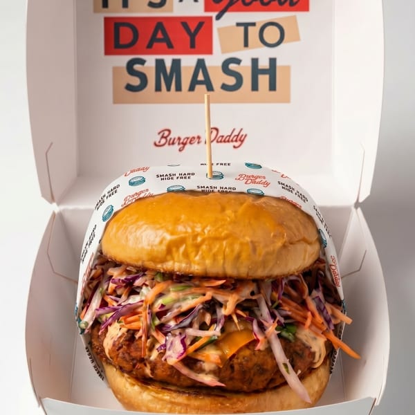 A Burger Daddy burger with slaw and sauce in an open takeaway box with "IT'S A Good DAY TO SMASH" printed inside.