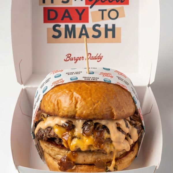 A Burger Daddy smash burger with cheese, caramelized onions, and sauce in a branded box.
