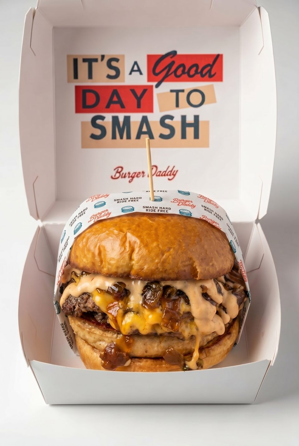 A Burger Daddy smash burger with cheese, caramelized onions, and sauce, in a branded box.